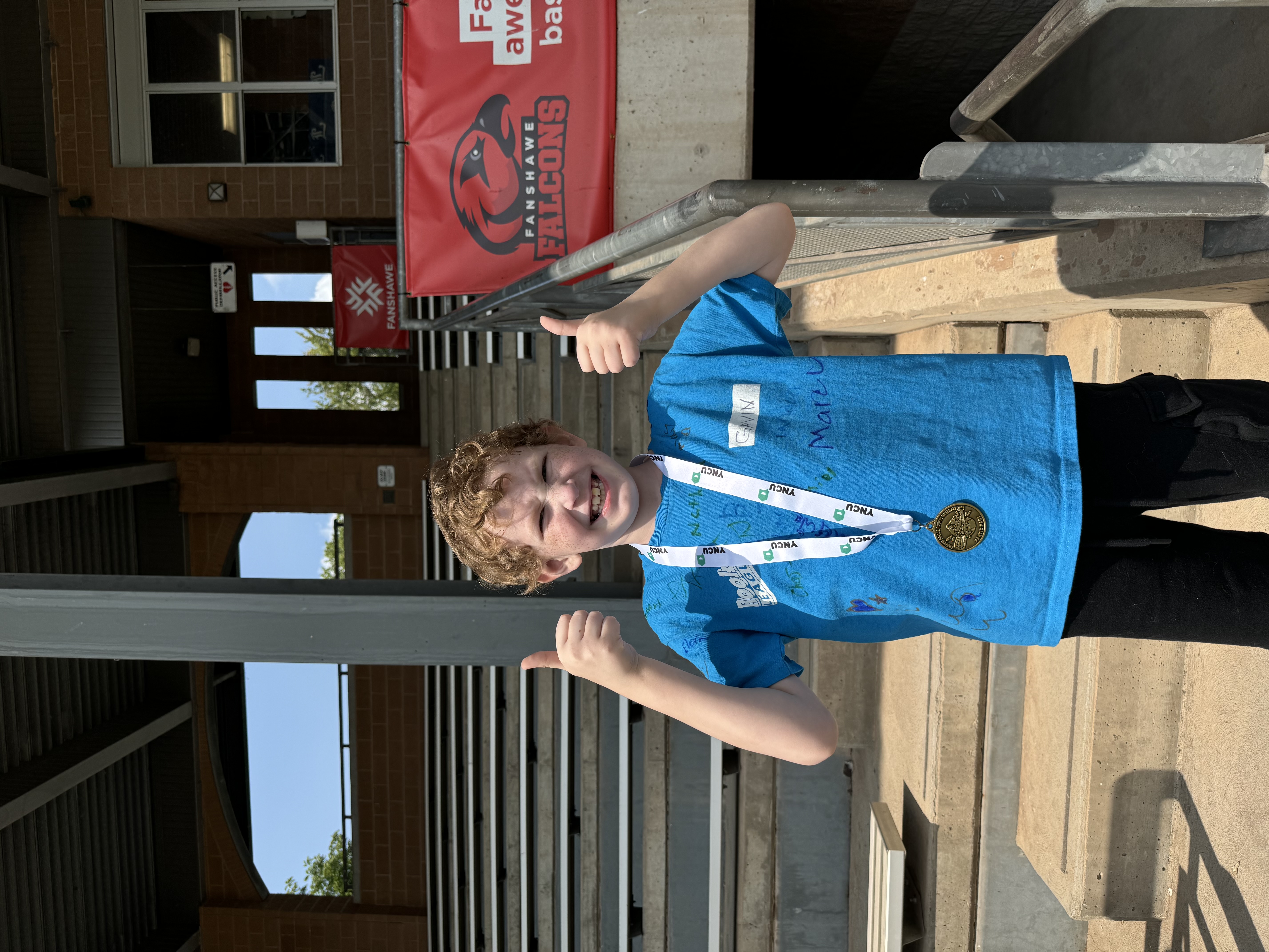 child showing off his medal and giving thumbs up sign