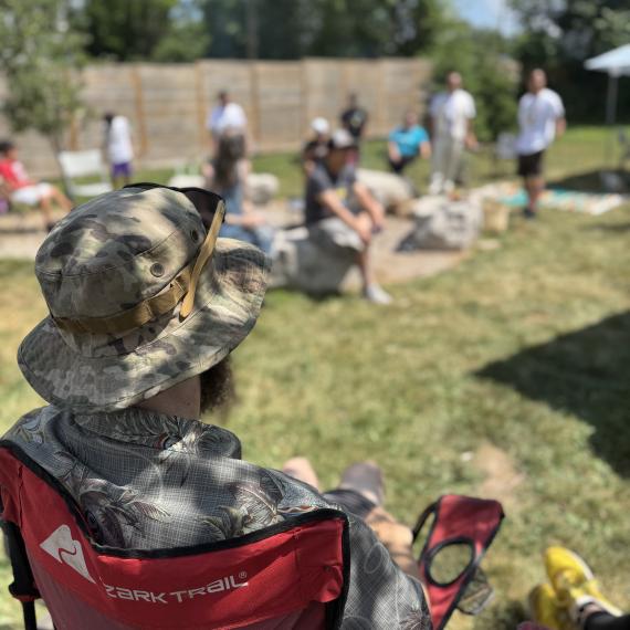 Man wearing camo, sitting on chair with people in the background